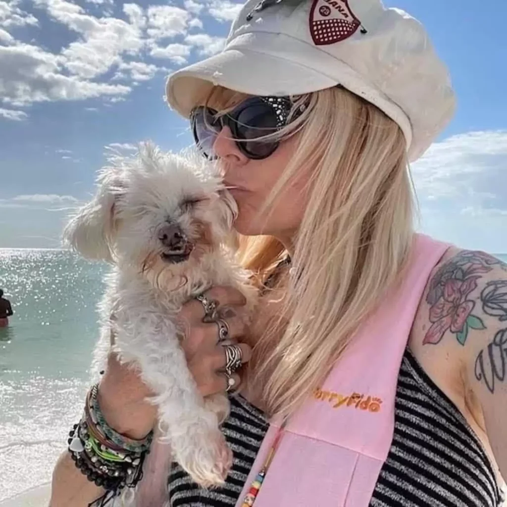 Woman kisses white dog on the beach.